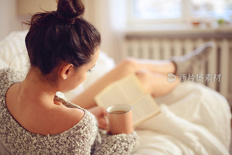 年轻女子一边喝热咖啡一边看书