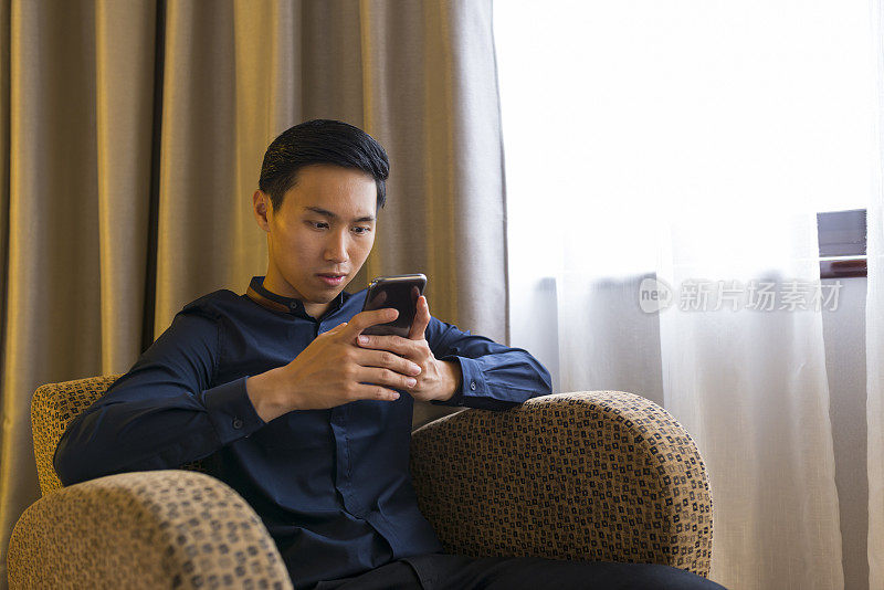年轻的亚洲商人用智能手机发短信