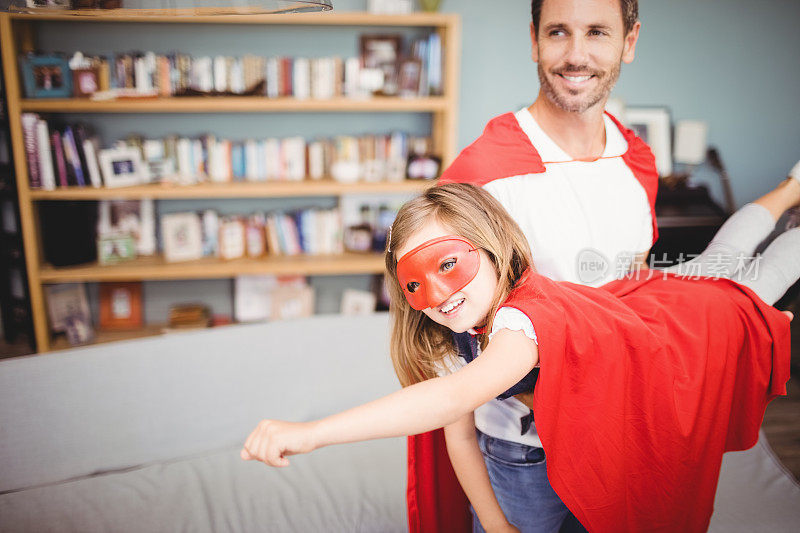 微笑的父亲抱着穿着超级英雄服装的女儿