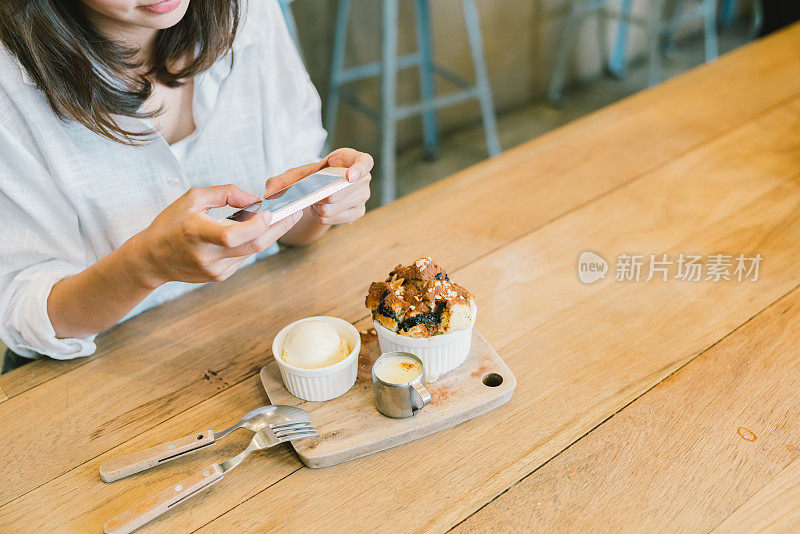 一个亚洲女孩在咖啡厅里拍摄巧克力烤面包蛋糕、冰淇淋和牛奶。甜点或食物摄影爱好。智能手机或手机拍照习惯概念。与复制空间