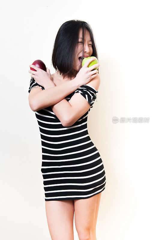 年轻美丽的亚洲女人咬着红绿苹果
