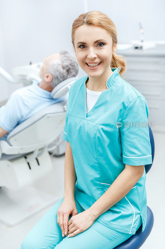穿着医疗制服的专业牙医坐在诊所里，对着镜头微笑