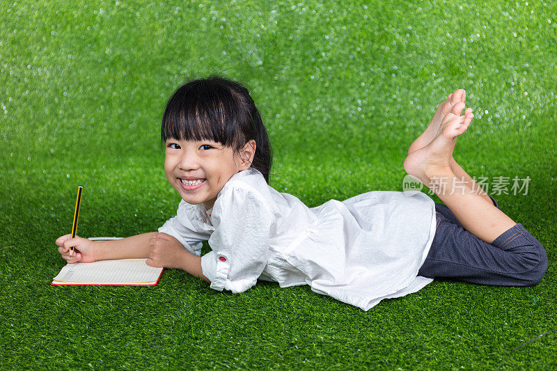 亚洲华人小女孩躺在草地上写字