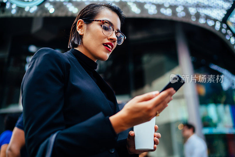 繁荣的女商人惊讶地看到好消息，一边走在街上一边阅读网站上的信息，带着眼镜的女商人微笑着查看智能手机上的通知，在市中心散步