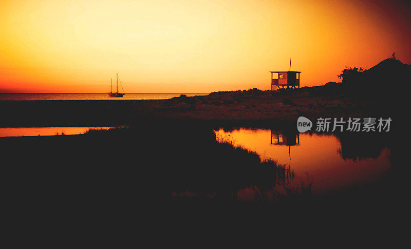 空鸵鸟海滩上的日落。法国科西嘉岛。瞭望塔和帆船的橙色天空和黑色剪影。