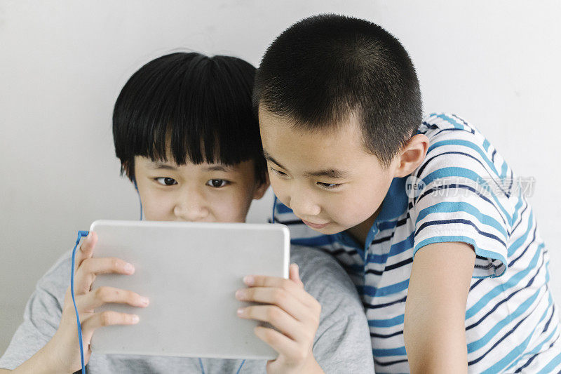 亚洲女孩和她的小弟弟用耳机玩触控板