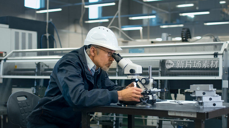 高级工程师正在工厂里用显微镜检查零件。