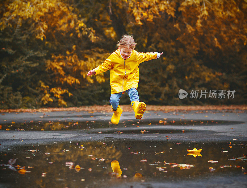 快乐的童女撑着伞，穿着胶靴在水坑里秋日漫步