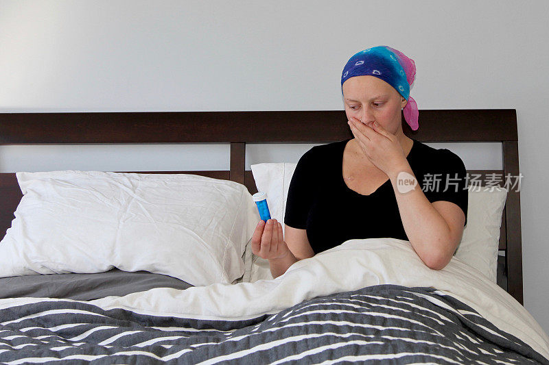 年轻的癌症患者坐在床上看着药瓶