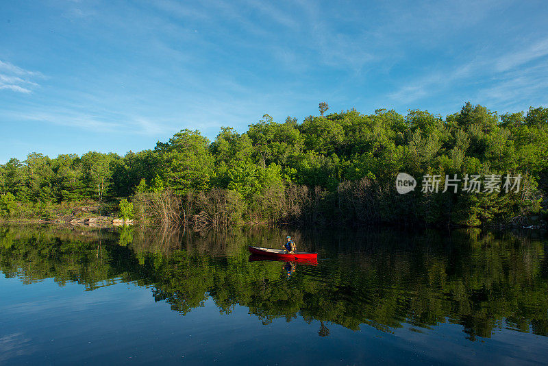 在加拿大，一个年轻人一大早在独木舟上钓鱼