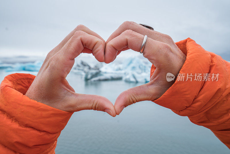 近距离观察冰岛冰川泻湖上做心形手指架的女人