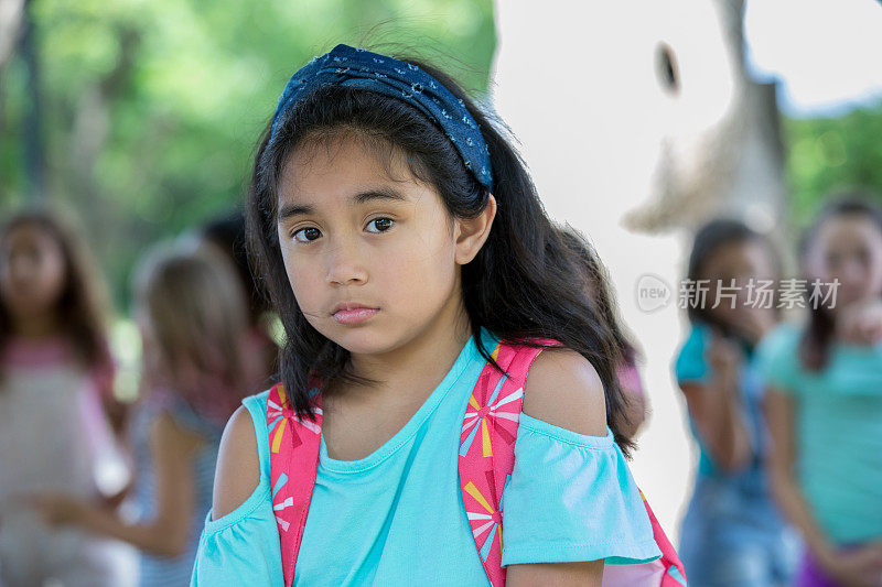 悲伤的亚洲小学女生看着镜头，而在背景的同学欺负她