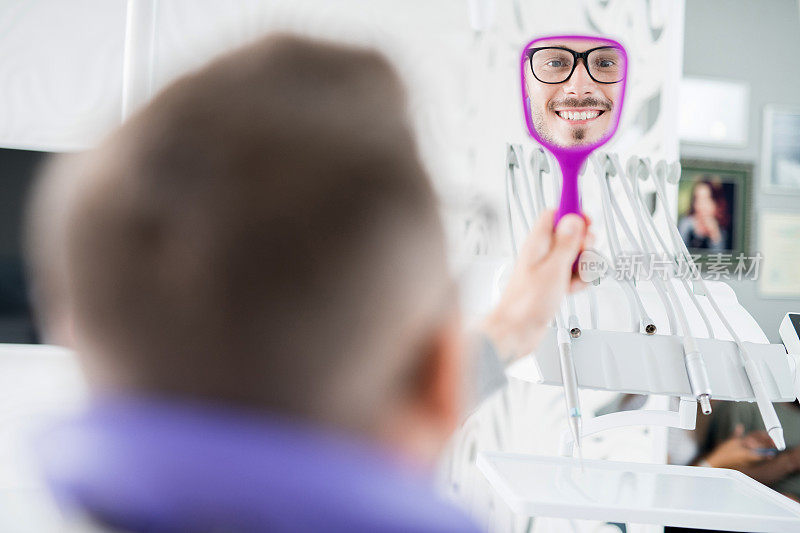 开朗英俊的年轻男病人，留着胡子，对看牙医时照镜子的工作感到满意