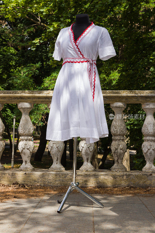 穿着白色衣服的人体模特。白色连衣裙，天然面料，红色元素。自定义裁剪。女士夏装配腰带