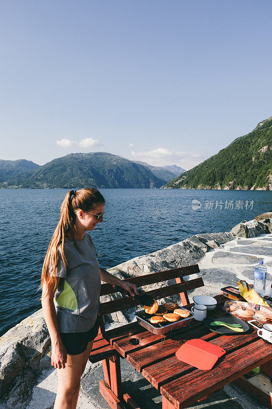 在挪威的峡湾风景中，一个女人在野餐时做汉堡