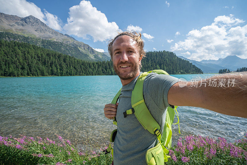 一个愉快的年轻人在一个美丽的山湖边自拍，享受一天的徒步旅行