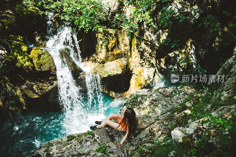 徒步旅行后，穿着泳衣的女人躺在瀑布附近的岩石上