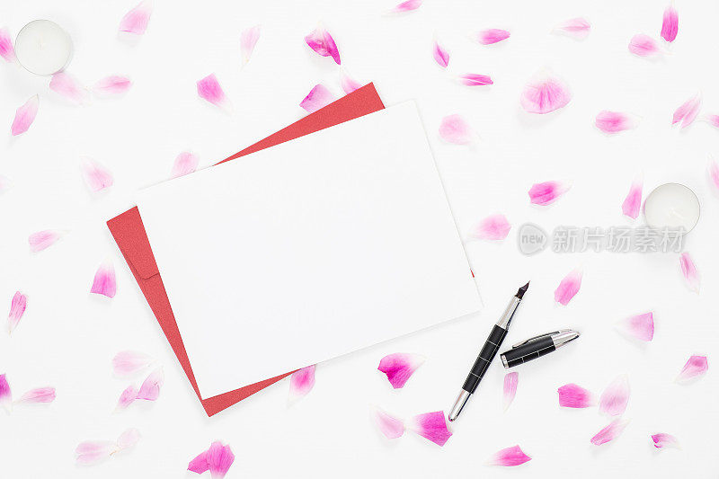 俯视图空白纸卡，红色信封，玫瑰花瓣在白色的背景。简约平铺风格构成，情书、贺卡概念。