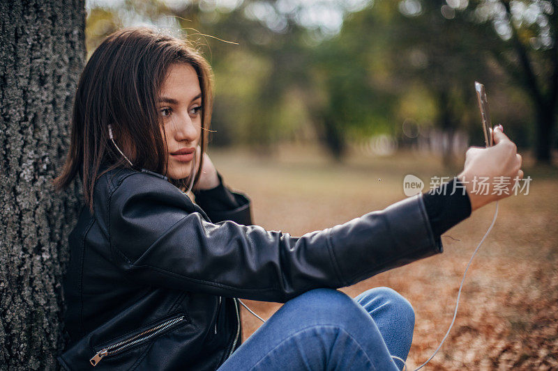 一个漂亮的年轻女子在公园里边自拍边听音乐。