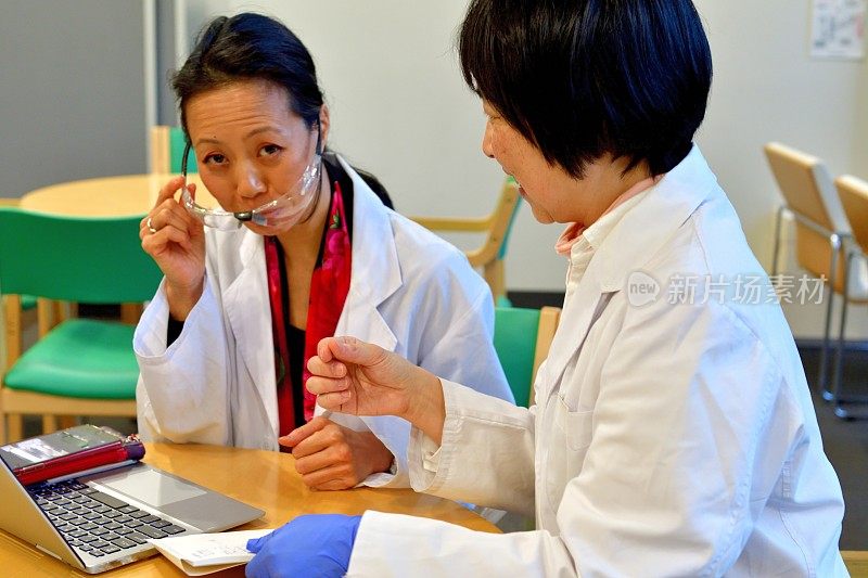 两个日本女人在个人电脑前比较她们的笔记