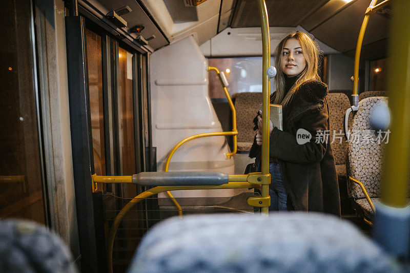 晚上乘公交车时拿着书的女乘客。晚上，女孩在窗口旁边的移动车辆上旅行