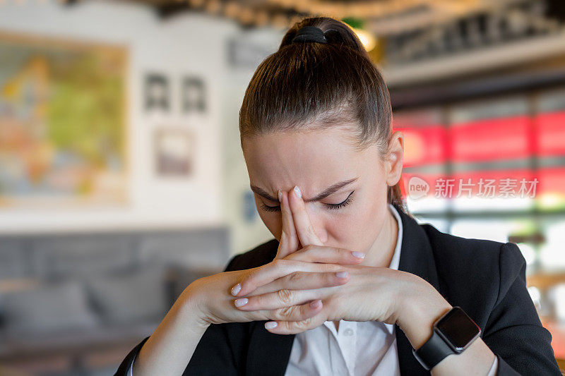 一个悲伤的年轻女人在咖啡馆里，双手合十，头靠着头