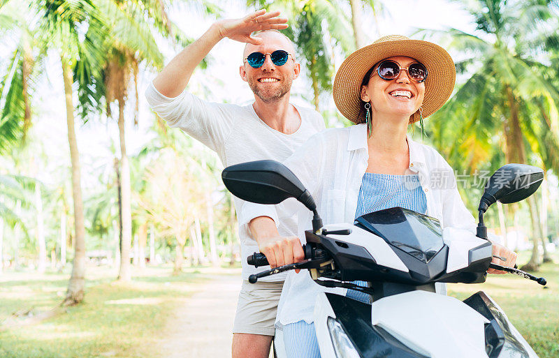 快乐的微笑夫妇旅行者骑摩托车踏板车在棕榈树下。泰国热带度假概念形象