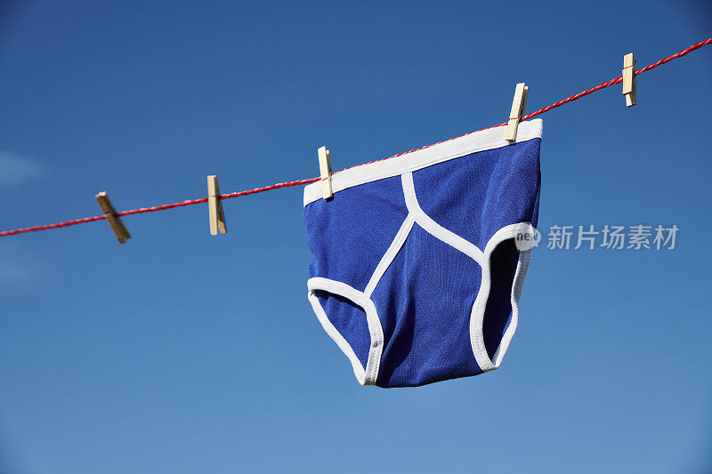 在一个晴朗的天空下，在晾衣绳上的复古亮蓝色y型前内裤。