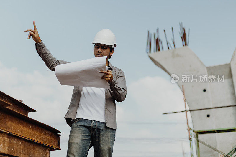 亚洲工程师男子戴安全帽和检查蓝图在施工现场，工程师建筑师施工现场规划概念
