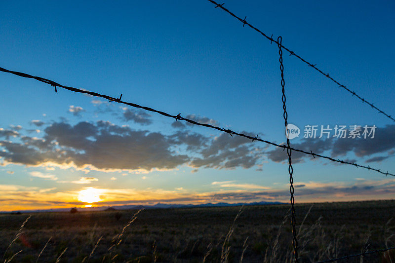 西南的夕阳透过铁丝网在远处与云层在地平线上