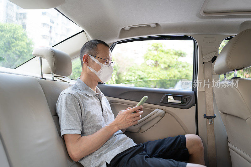 戴着防护口罩的亚洲男性员工在车里独自使用手机