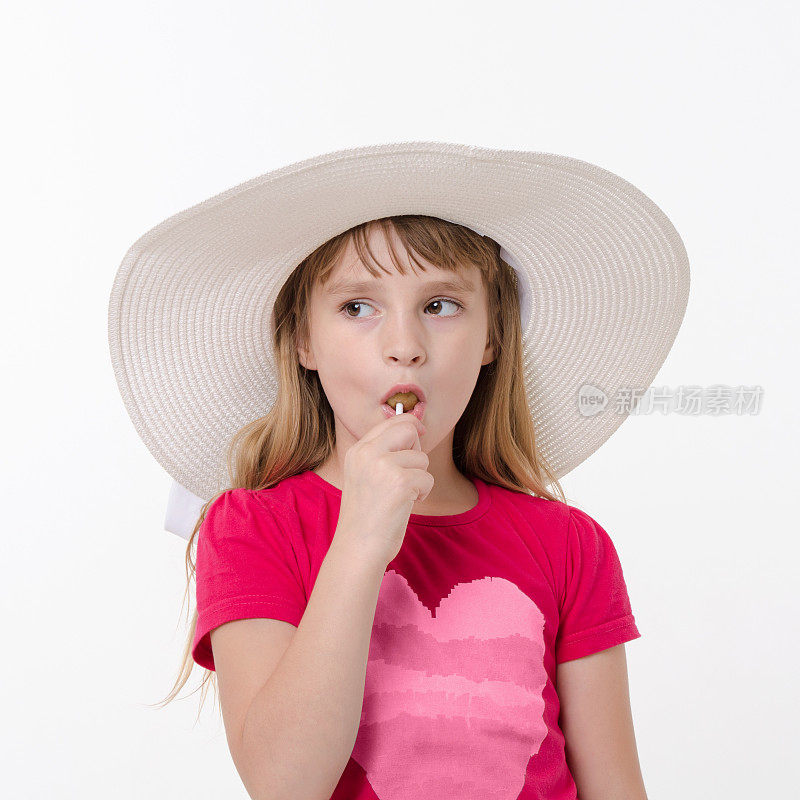 小女孩戴着大帽子吃着棒棒糖，白色背景上的工作室肖像