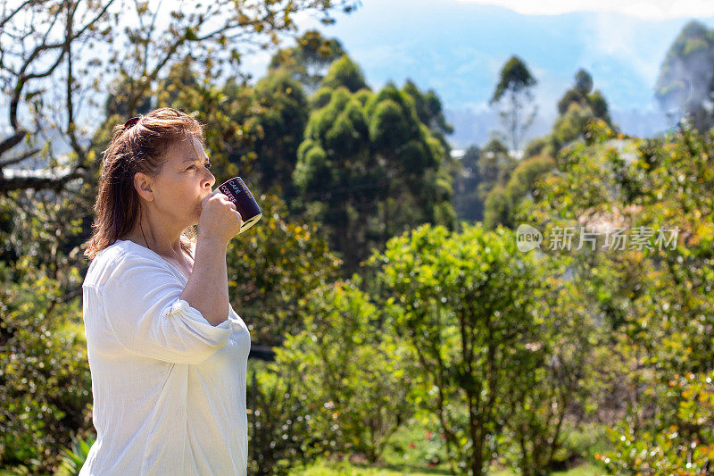 放松的女人在早上喝咖啡，周围的自然