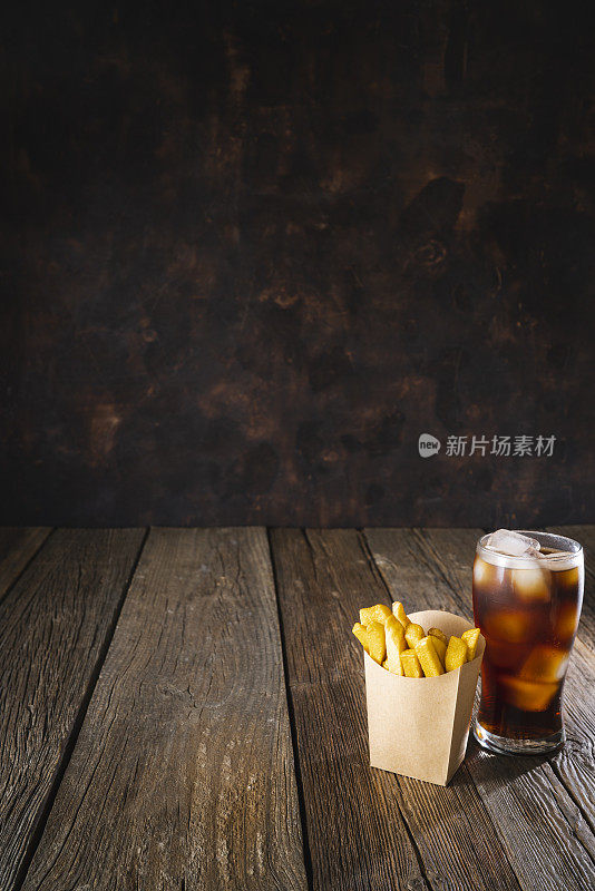 深色木桌上放着牛皮纸盒子装的可乐苏打杯和一次性薯条