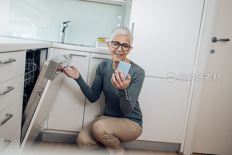 一个成熟的女人正在准备她的餐具，并在使用智能手机