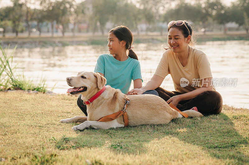 亚洲女儿和母亲带着拉布拉多寻回犬坐在公园里