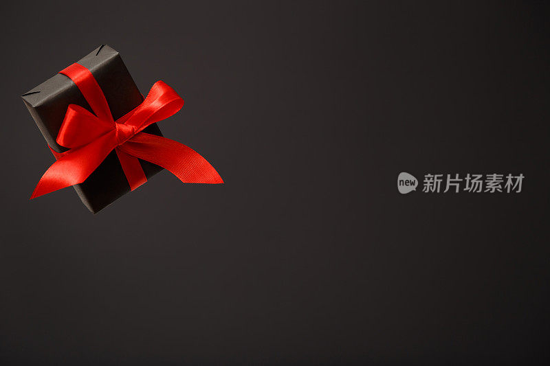 美丽的飞行黑色礼品盒与红色蝴蝶结浮动在空气中黑色的背景。黑色星期五促销，圣诞节促销，折扣概念。情人节。父亲节