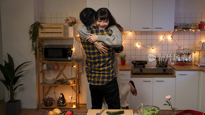 慢镜头:一个亚洲男人拥抱并举起他的女朋友，庆祝情人节，晚上在家里一个装饰好的厨房里