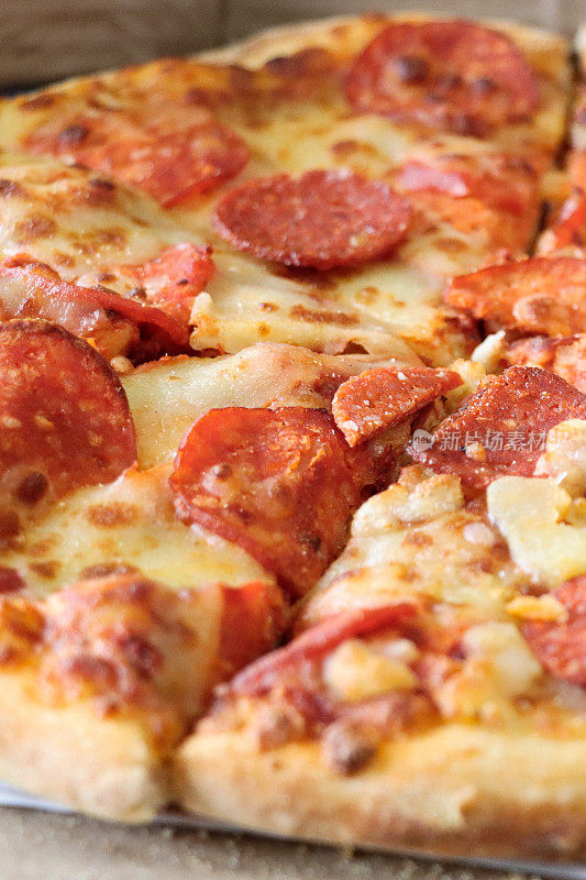 全帧图像的切片意大利辣香肠披萨在纸板外卖披萨盒，融化的金色水牛马苏里拉奶酪和丰富的番茄番茄沙司，重点在前景