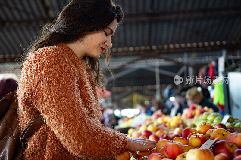 一名年轻女子在当地食品市场购买新鲜水果和蔬菜的照片