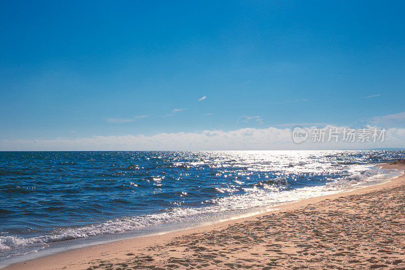 蓝色的大海在阳光下波光粼粼，沙滩和夏天的蓝天