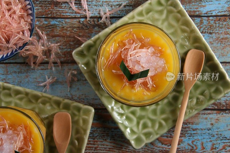 冰芒果蜜柚甜点在老式玻璃和木勺，在花压花的方形盘子