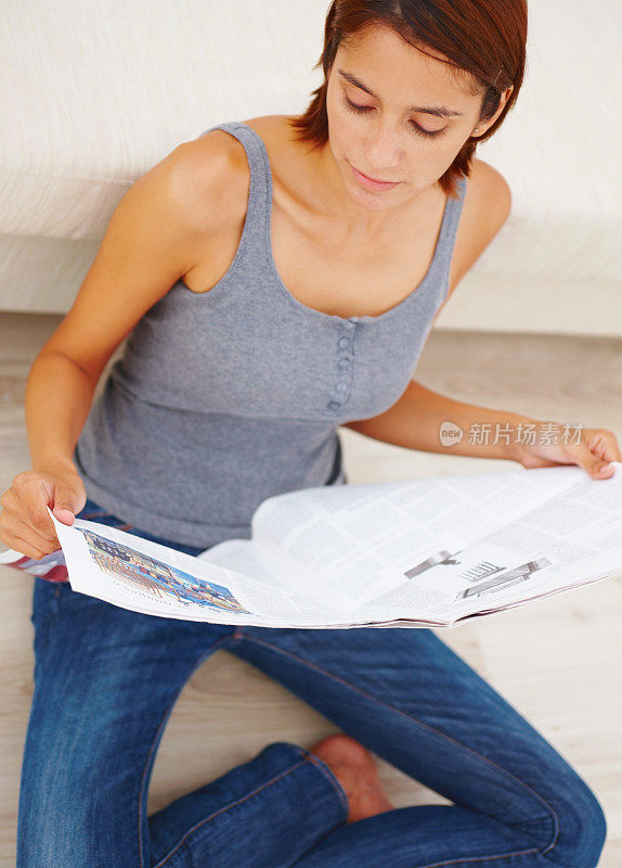 一个年轻女子坐在沙发旁看报纸