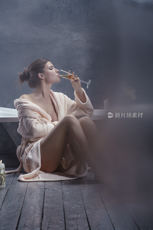 美丽的女人放松在浴袍拿着一杯香槟