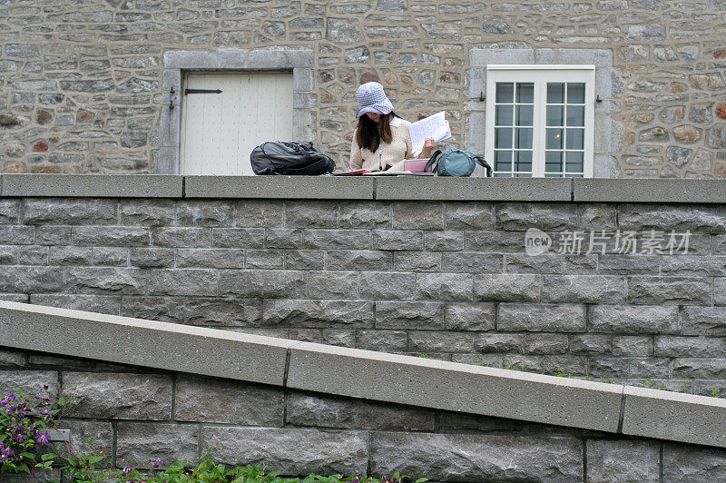 年轻女子在一堵石墙上学习。