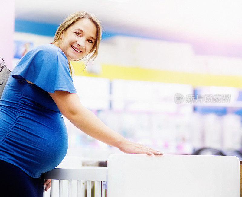 孕妇微笑着，在婴儿商店挑选婴儿床