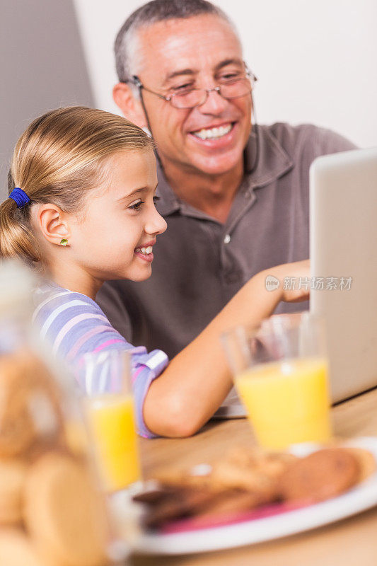 微笑的女孩看着笔记本电脑和爷爷
