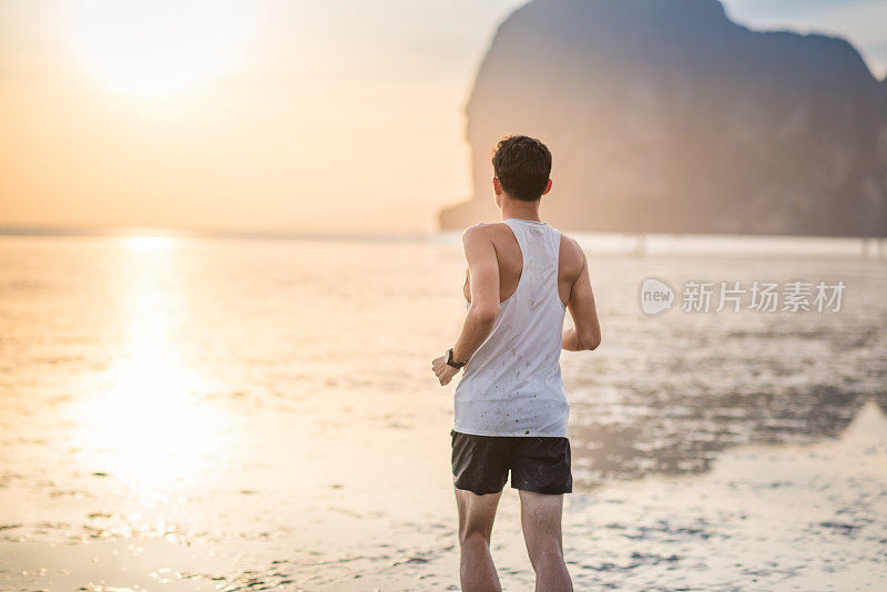 年轻的亚洲男子在海滩上奔跑，夕阳为背景