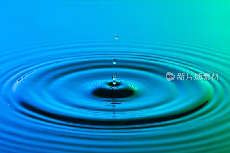 水滴近距离与同心涟漪在五颜六色的蓝色和绿色表面