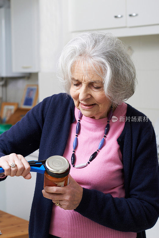 年长妇女用厨房助手打开罐盖